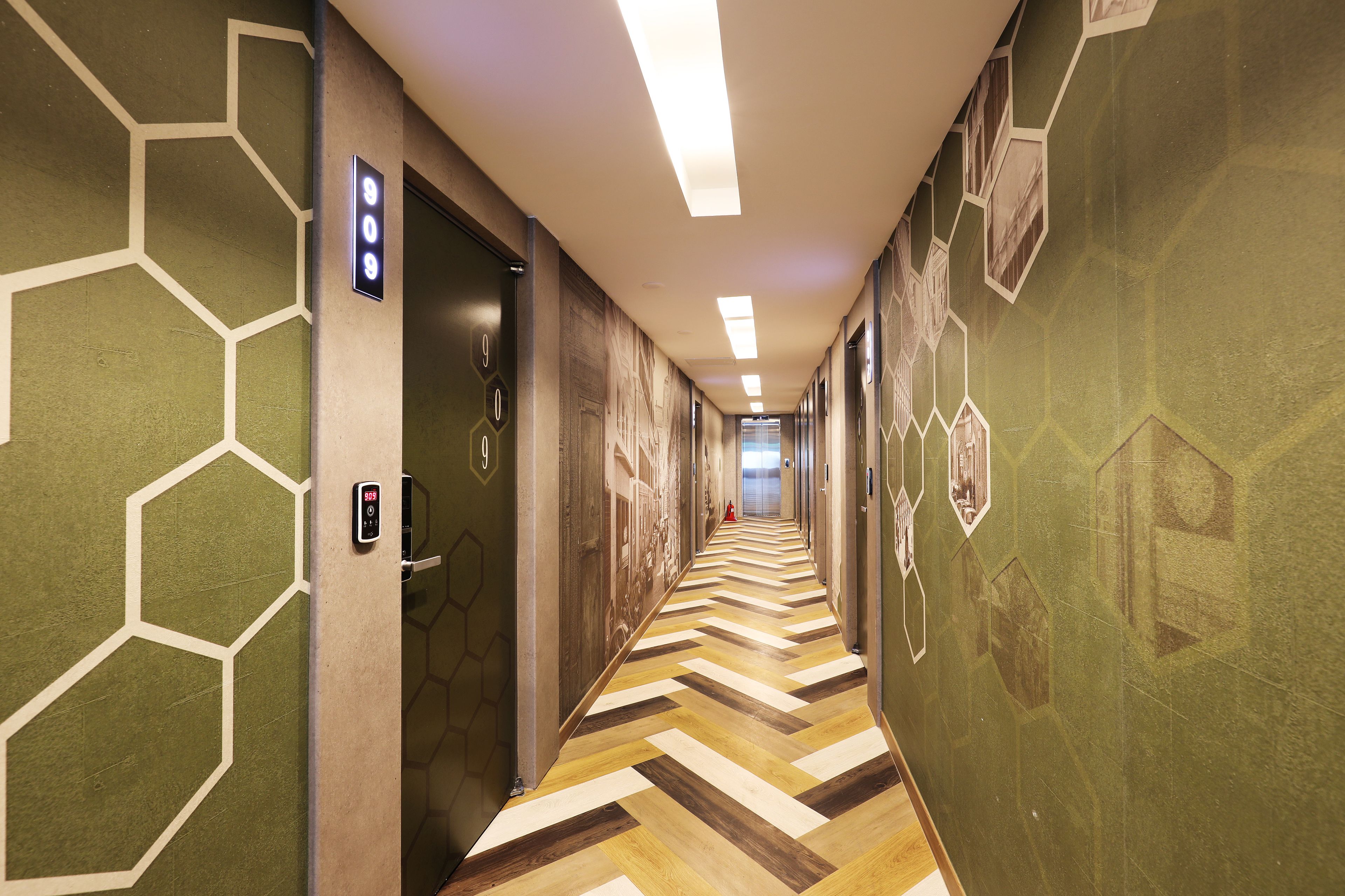 A hallway with a geometric patterned wall, a chevron-patterned floor, and a series of doors with numbers.