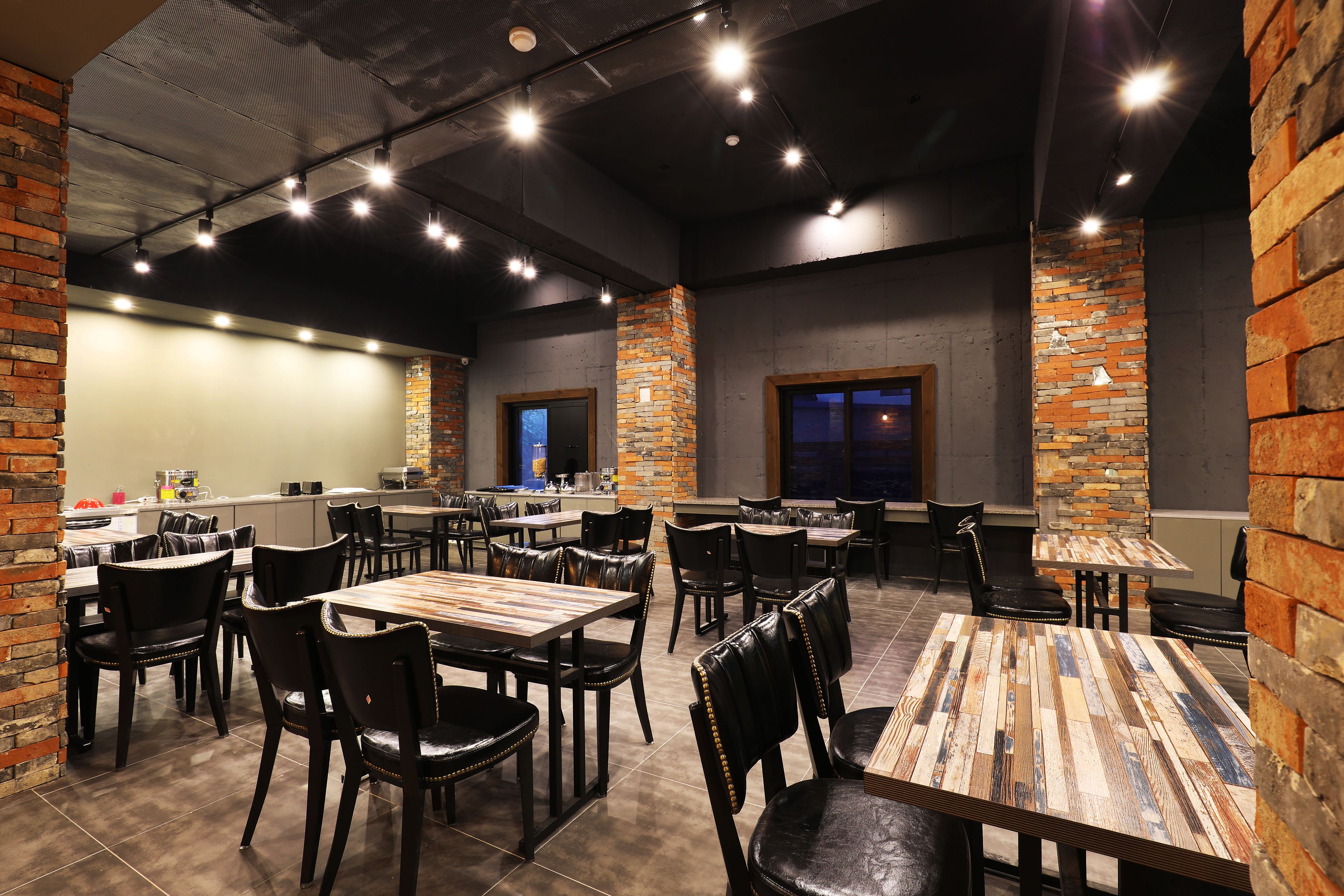 A restaurant with brick walls, wooden tables, and black leather chairs.