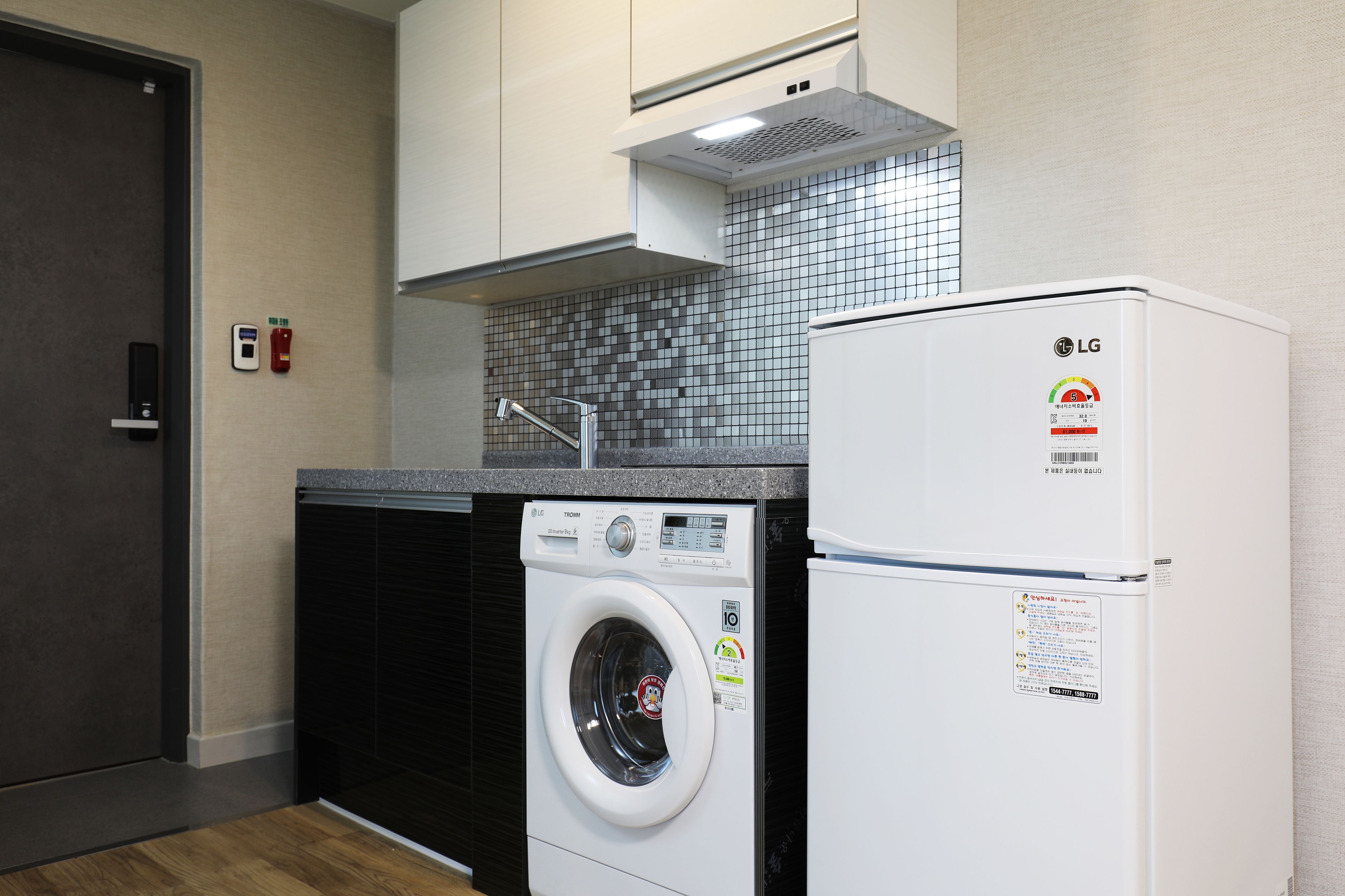 A compact kitchen with a washing machine, a refrigerator, and a tiled backsplash.