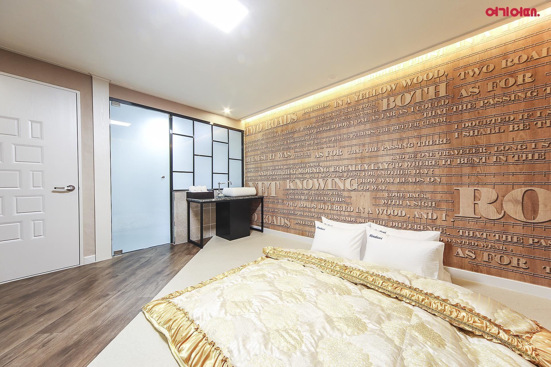 A bedroom with a large bed, a nightstand, a mirror, and a wall with engraved text.