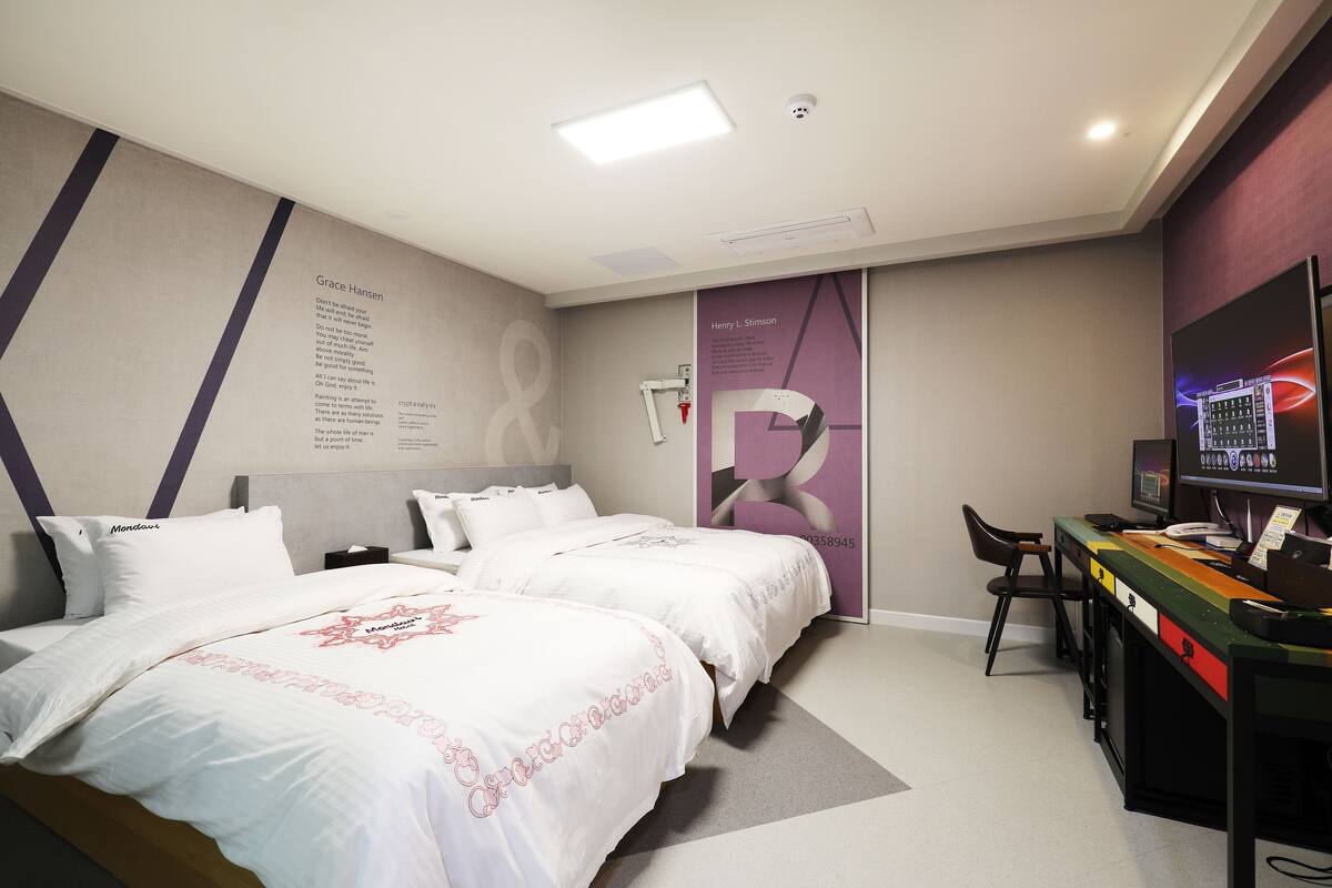 A hotel room with two beds, a desk with a computer, and a TV.