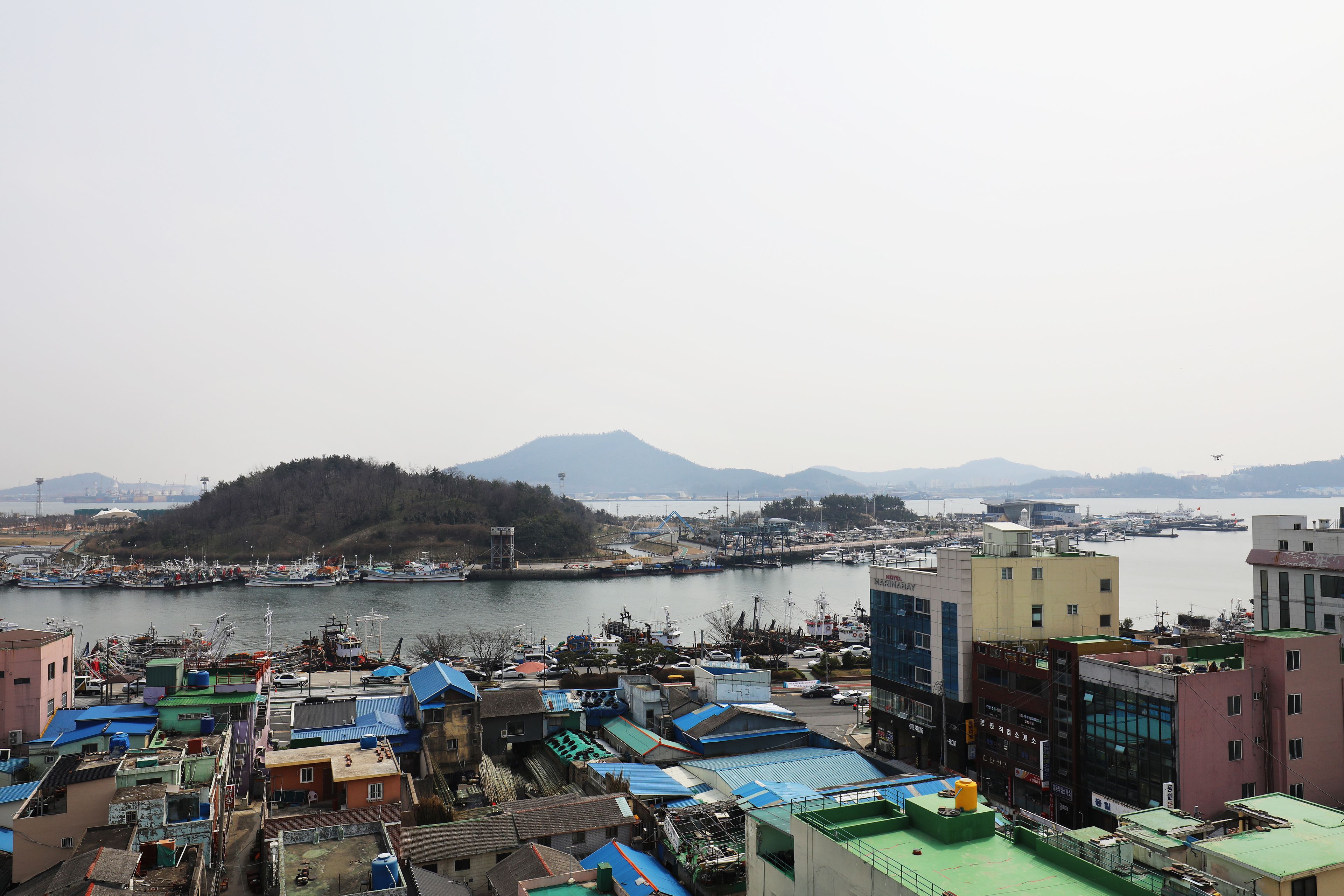 A coastal cityscape with a marina, buildings with blue roofs, and a distant mountain.