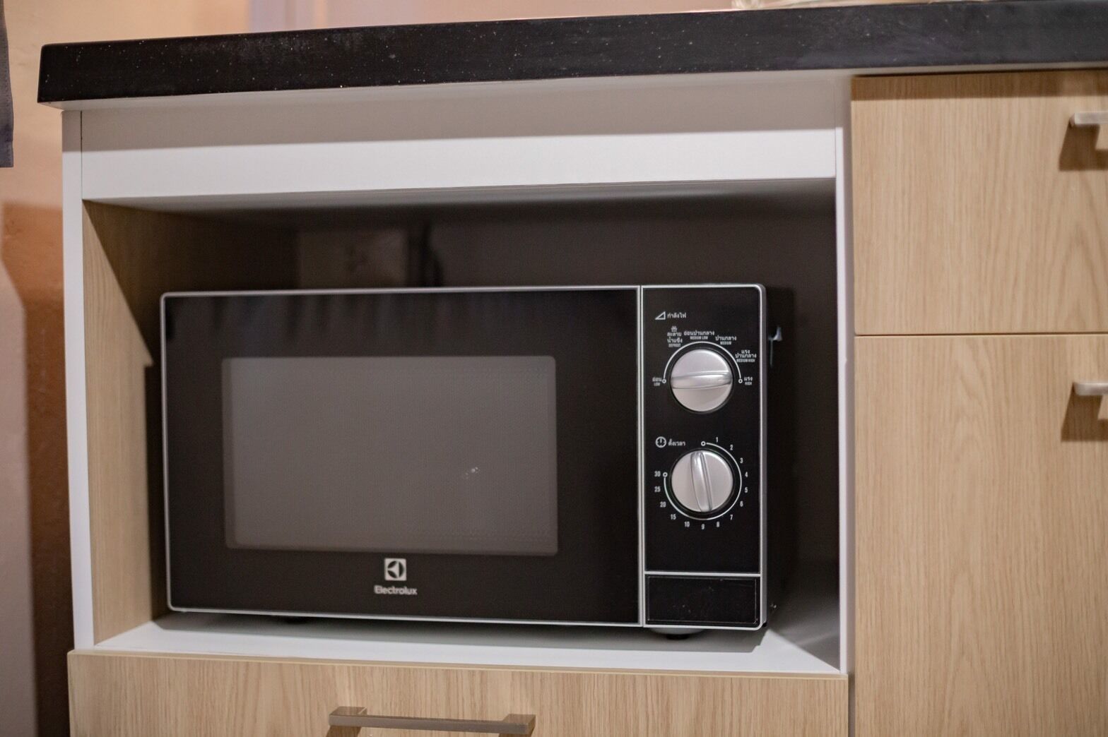 A black Electrolux microwave oven with two control knobs and a digital display, housed in a wooden cabinet with a black countertop above.