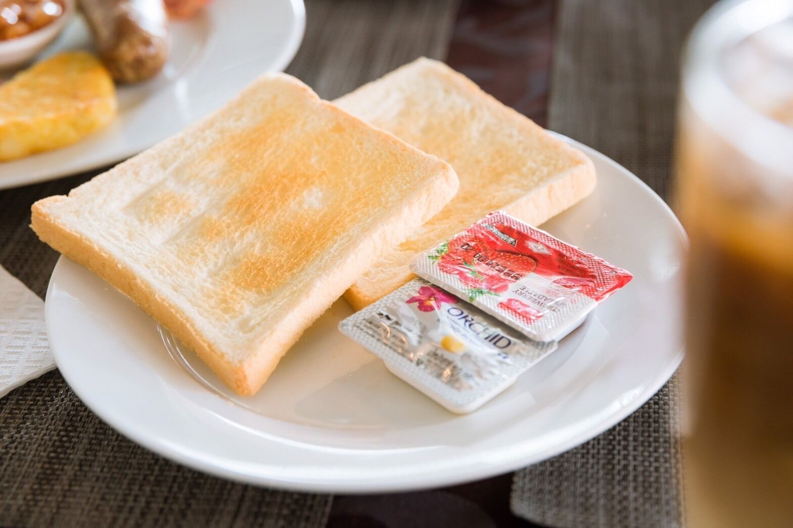 Two slices of toast on a white plate with two packets of sugar and jam.