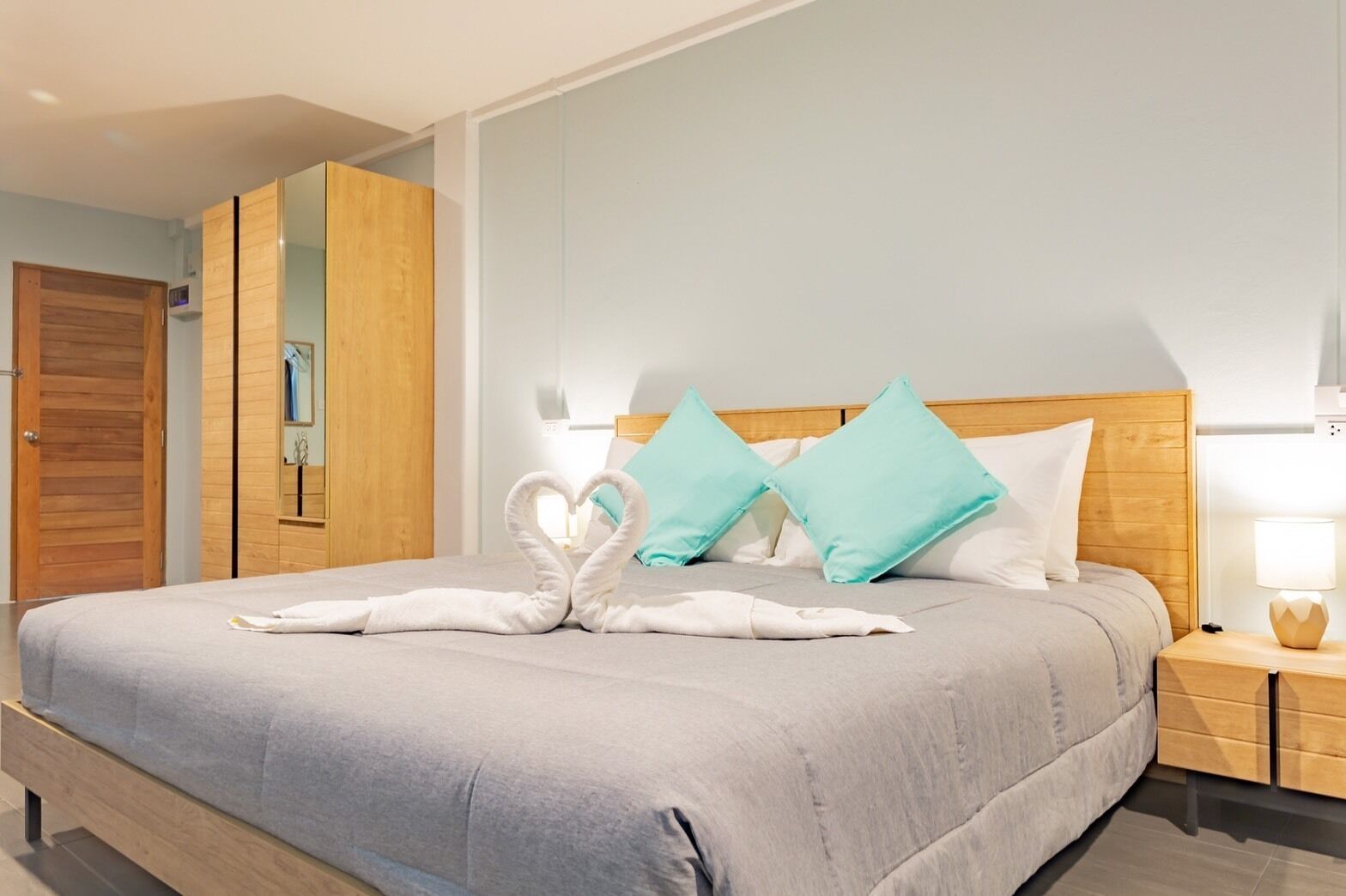 A hotel room with a bed, a wooden wardrobe, a nightstand, and a wall-mounted mirror.