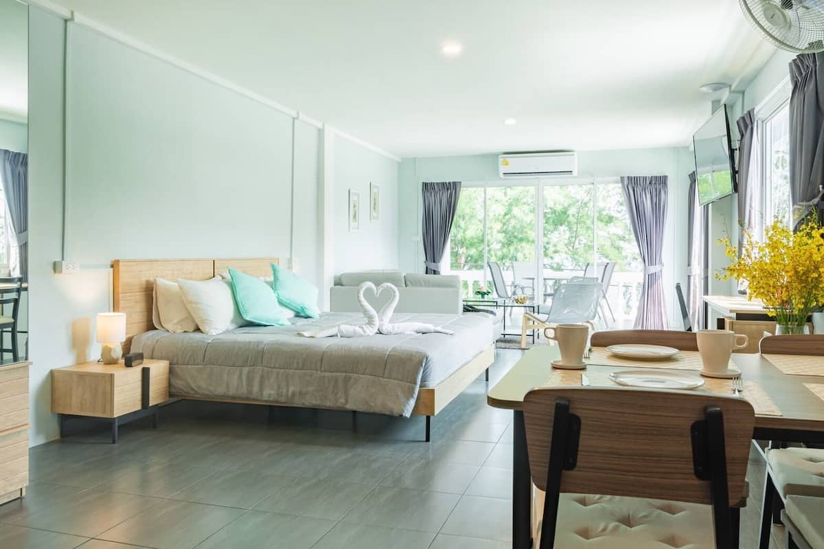 Habitación de hotel moderna con una cama grande, mesitas de noche, un área de comedor y vistas a zonas verdes.