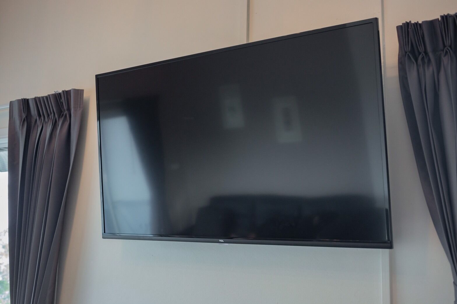 A flat-screen TV mounted on a wall with dark curtains on either side.