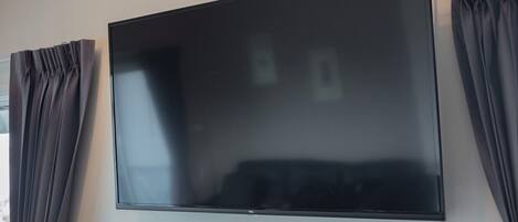 A flat-screen TV mounted on a wall with dark curtains on either side.
