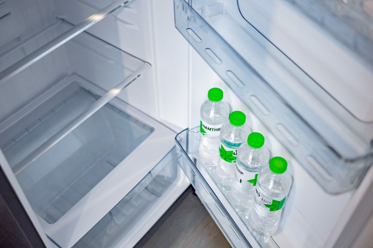 An open refrigerator with clear shelves and a water dispenser containing four bottles.
