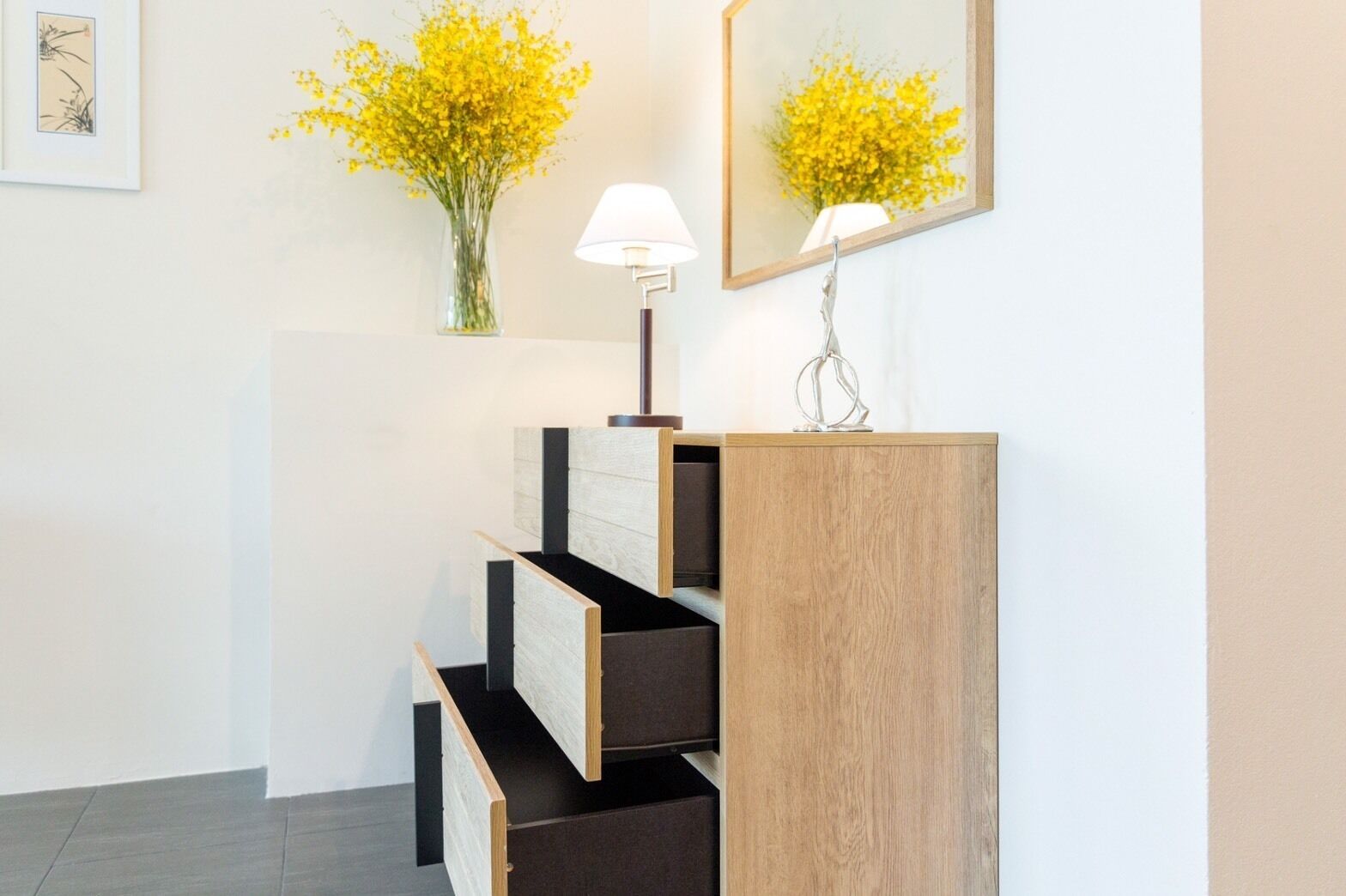 Un intérieur moderne avec un escalier en bois, un miroir mural reflétant des fleurs jaunes et un lampadaire.