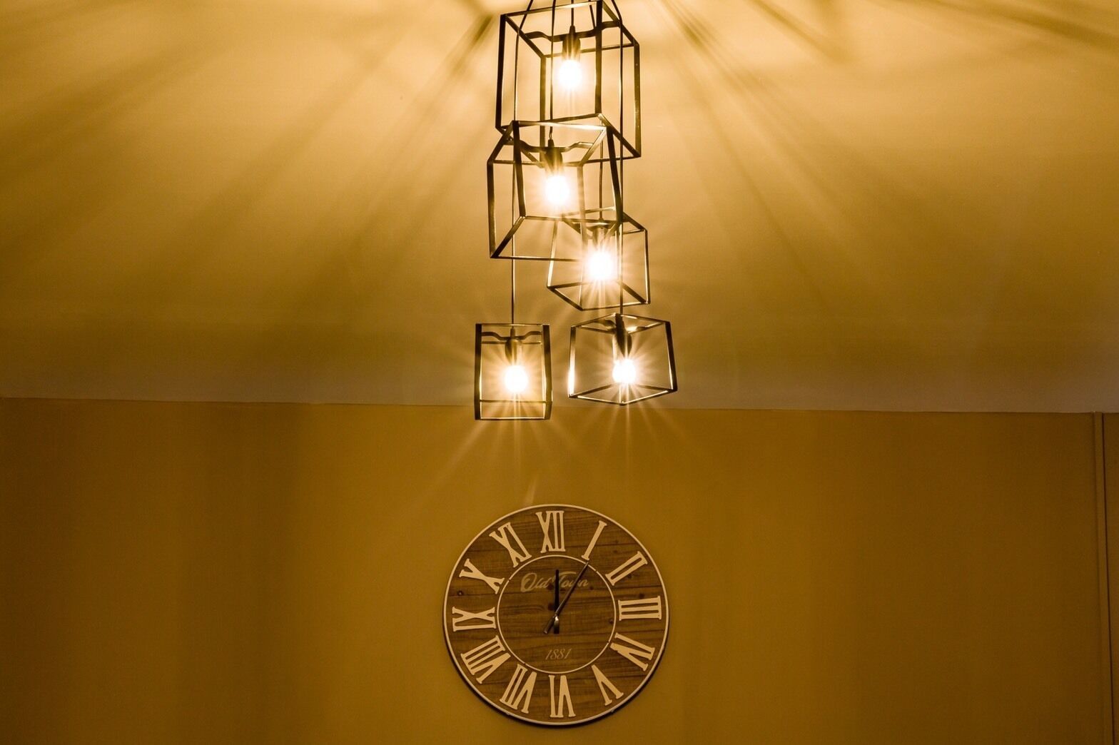A wall-mounted clock with Roman numerals and a modern geometric light fixture above it.