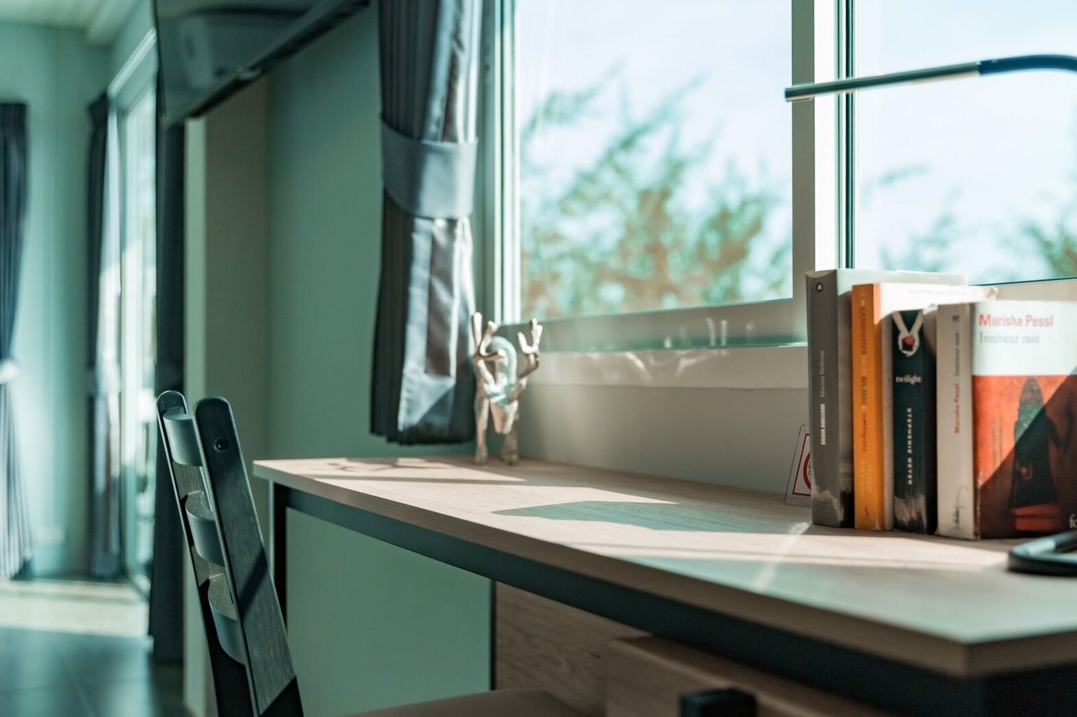 A desk with a chair, a window with curtains, and a bookshelf with books.