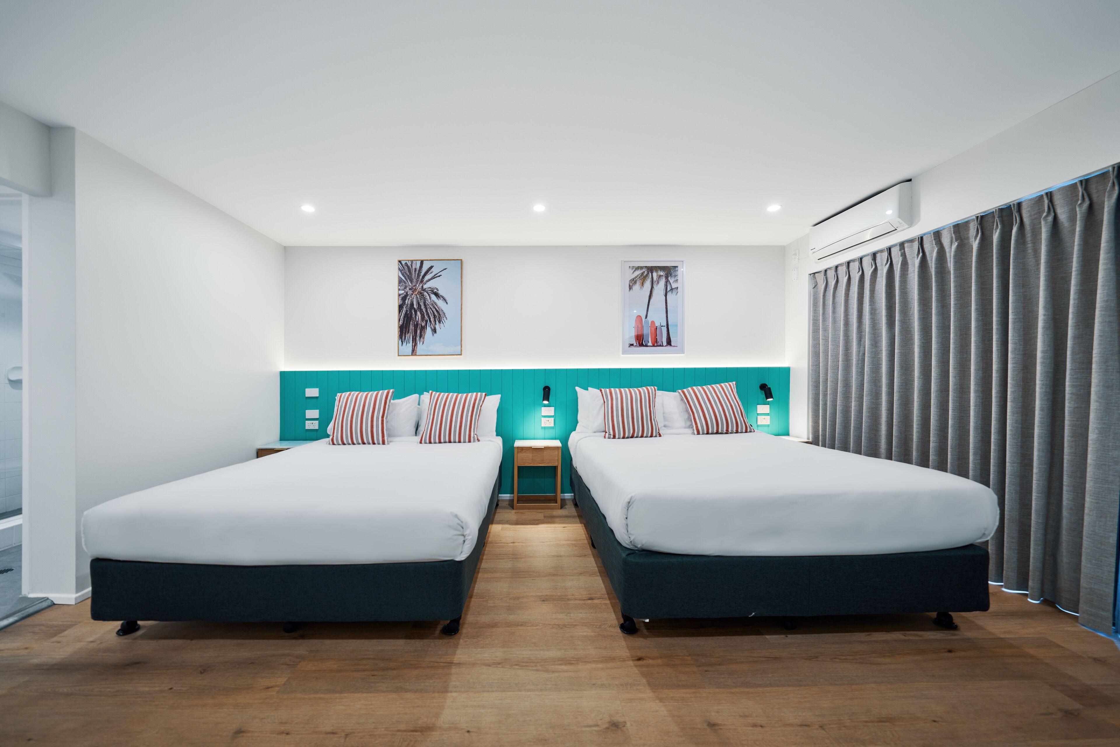 Une chambre d’hôtel avec deux lits, des murs d’un bleu-vert vif et un plancher en bois.