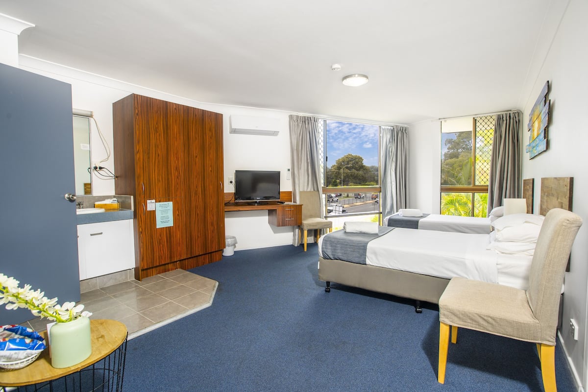 A hotel room with a bed, desk, chair, and a view of the outdoors.