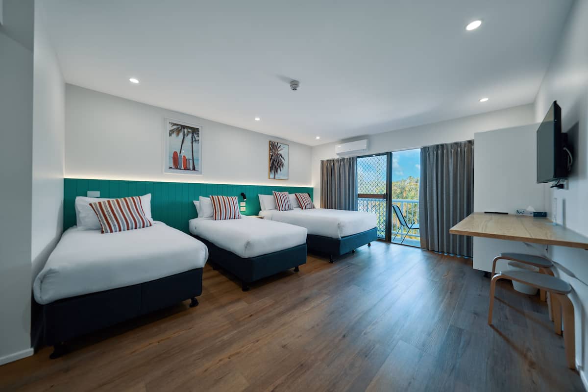 A hotel room with three beds, a desk, and a TV.