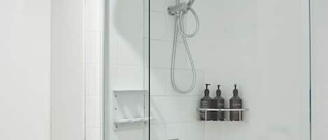 A modern bathroom with a glass-enclosed shower, white tiles, and a toilet visible to the left.
