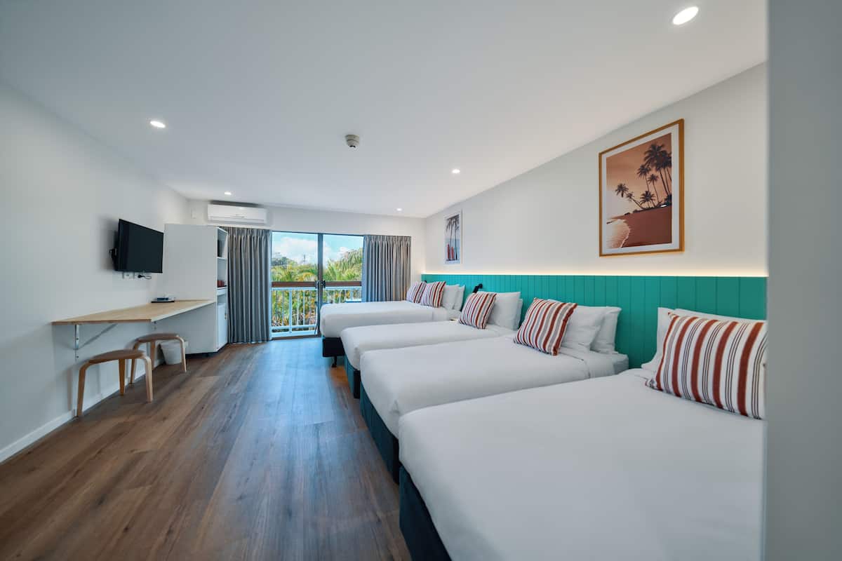 A hotel room with four beds, a desk, a TV, and a balcony with a view.