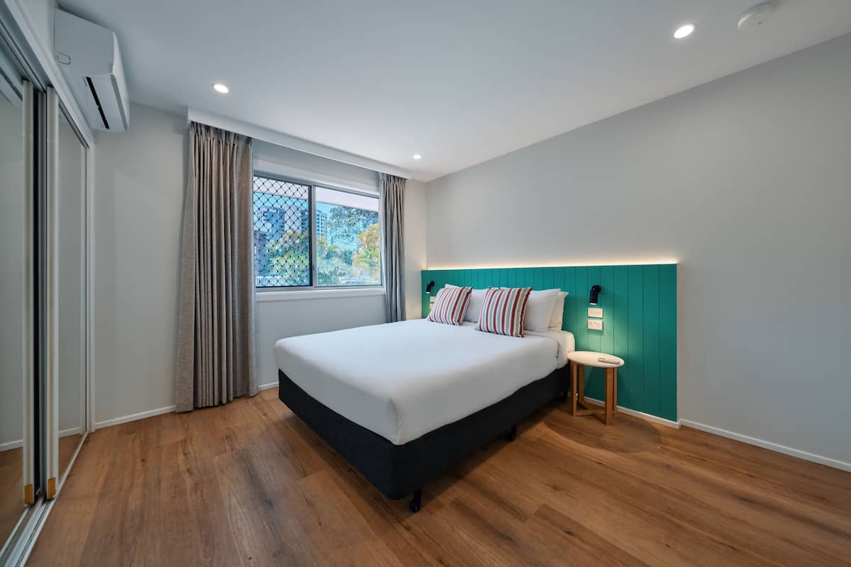 A modern bedroom with a large bed, a nightstand, a teal accent wall, and a window with curtains.