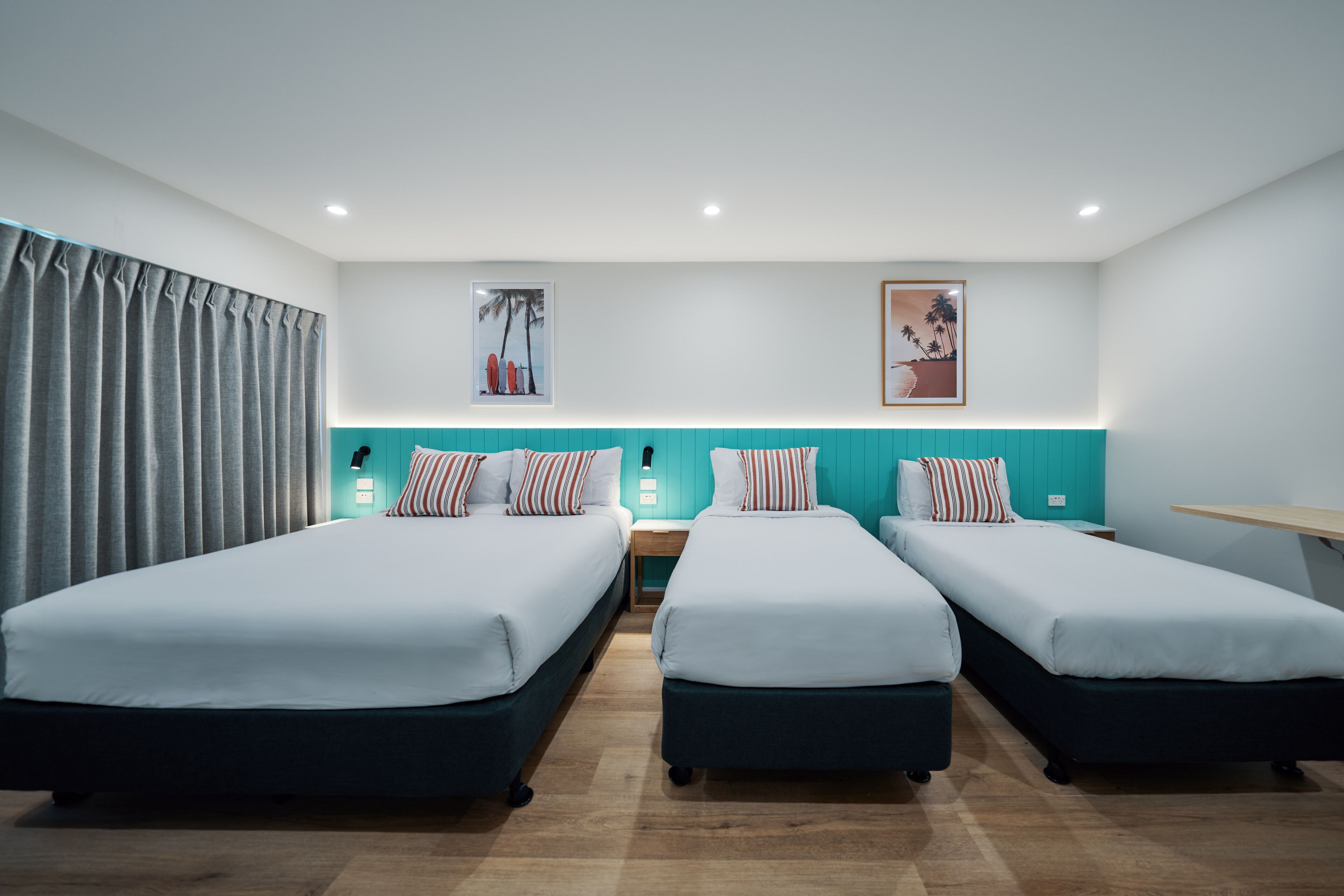 Habitación de hotel con dos camas individuales, un escritorio, una silla, una mesita de noche y un ventanal grande con cortinas.