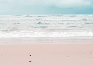 A beach with a pink sand shore and waves in the background.