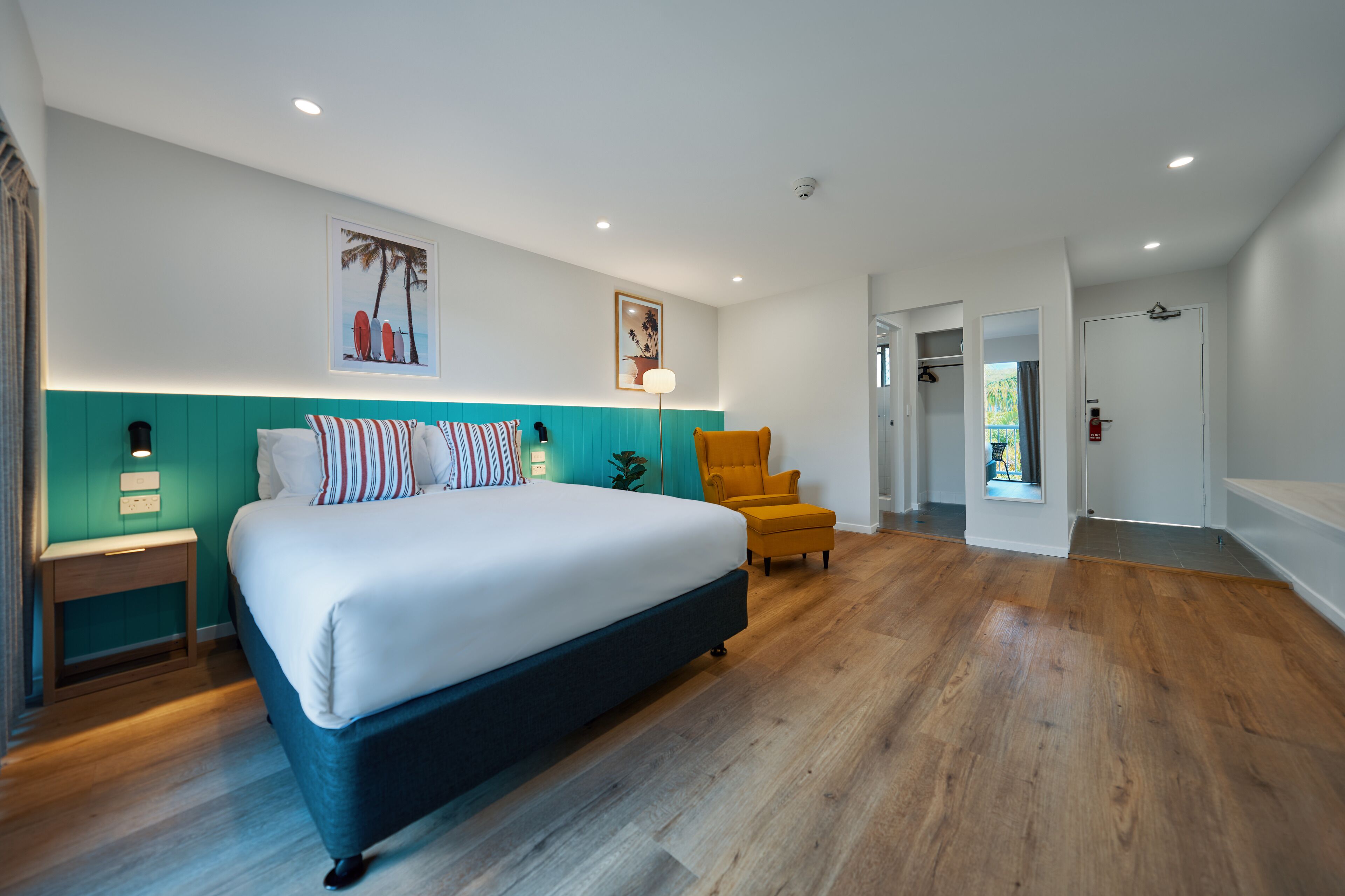 A modern bedroom with a large bed, a teal accent wall, and a wooden floor.
