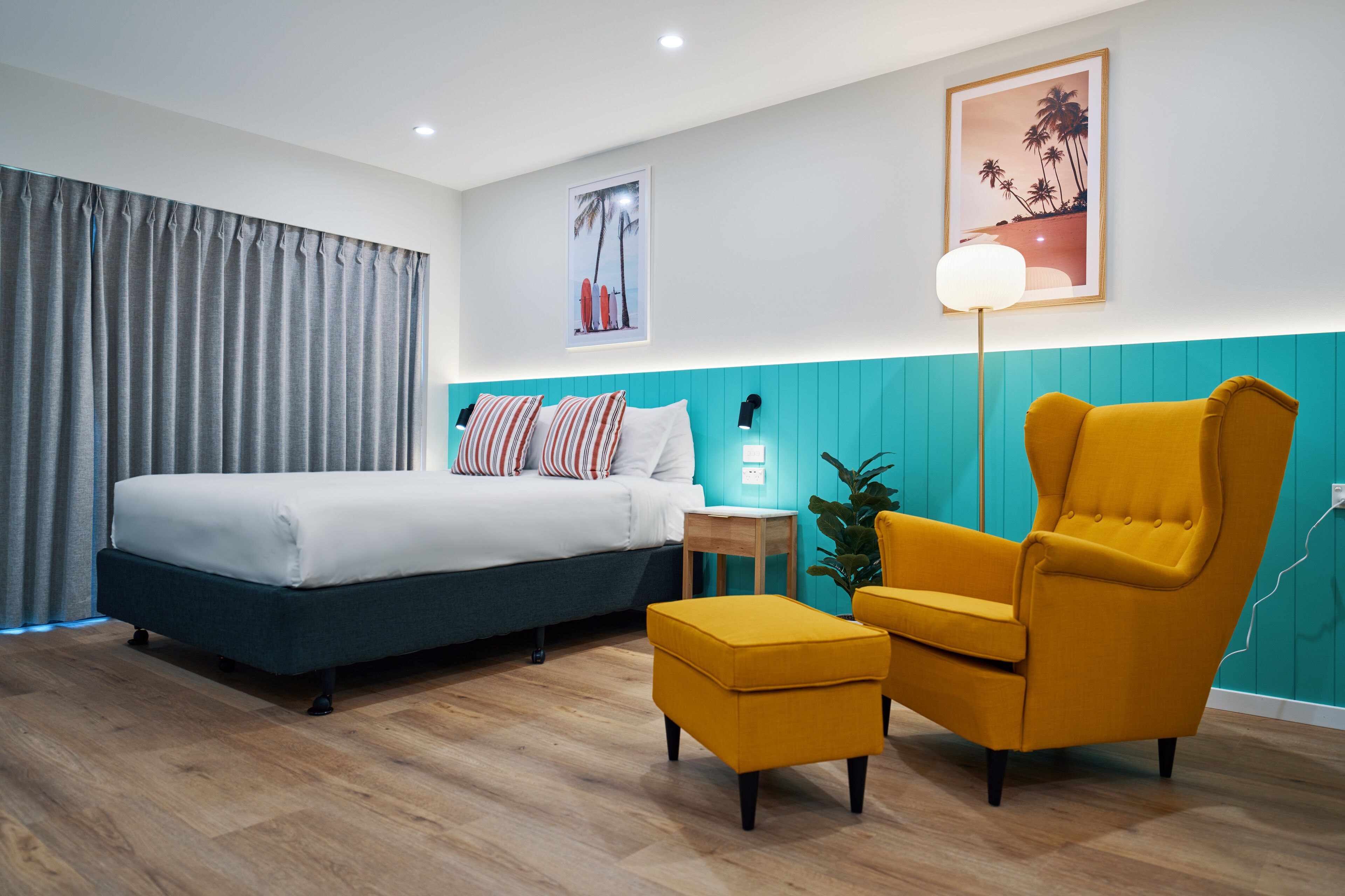 A modern hotel room with a bed, a yellow armchair, a small table, and a potted plant.