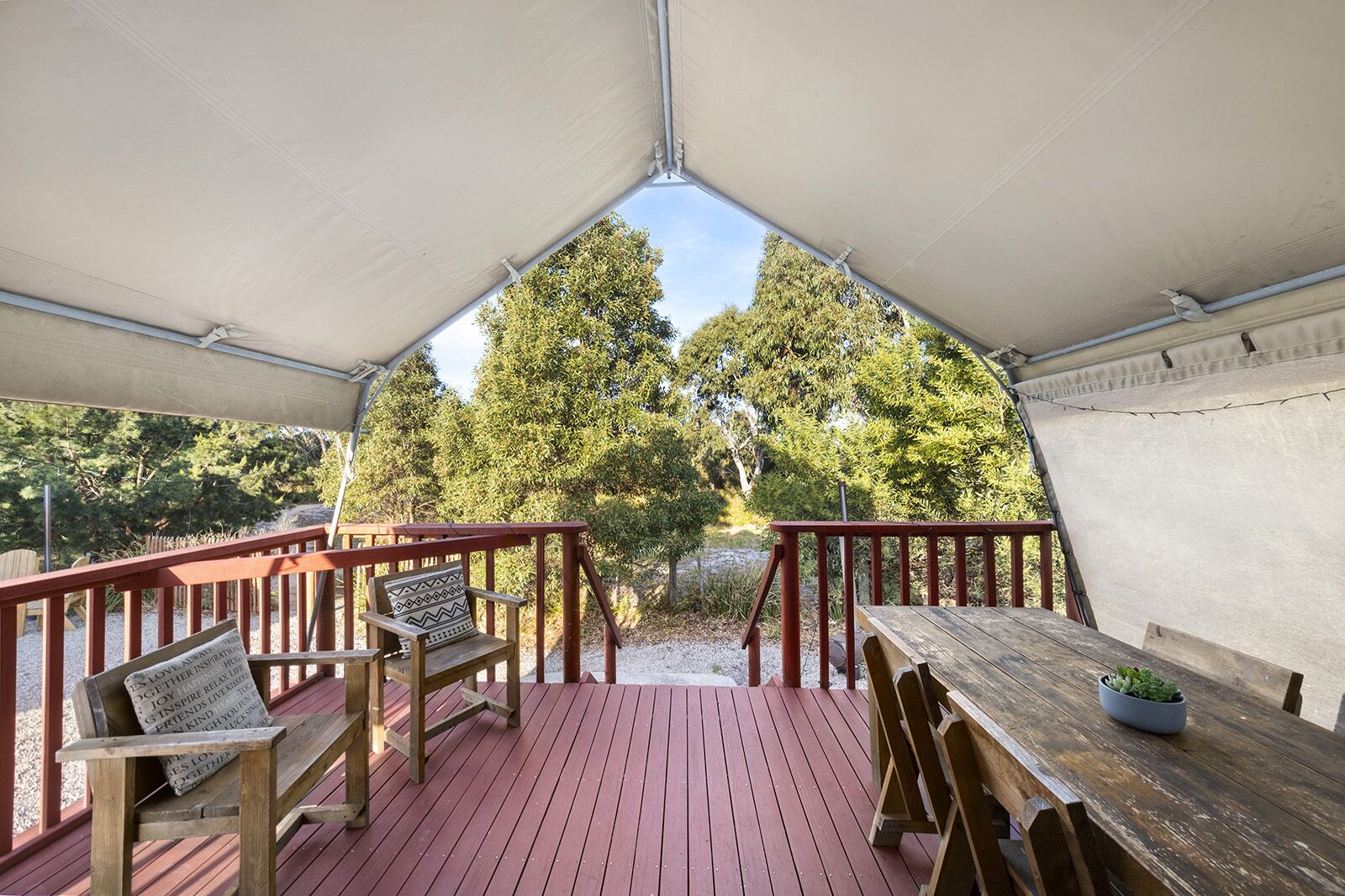 Una terraza techada con mobiliario de madera y vistas a árboles.