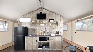 A compact kitchen with a built-in refrigerator, a sink, and wooden cabinetry. There is a flat-screen TV mounted on the wall, and a window providing natural light. - Scamander Sanctuary Holiday Park (Scamander)