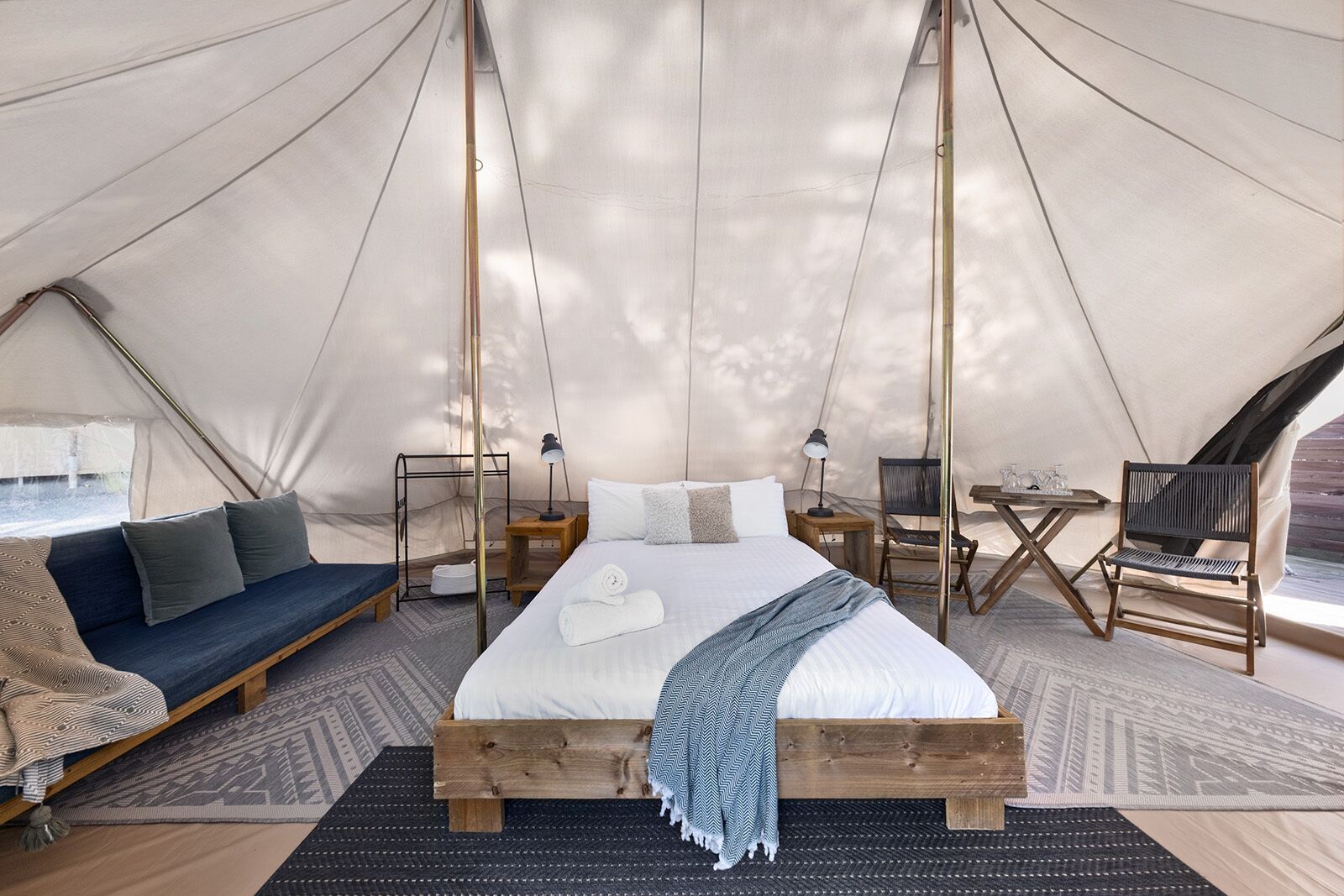 A tented accommodation with a bed, seating area, and a table with chairs.