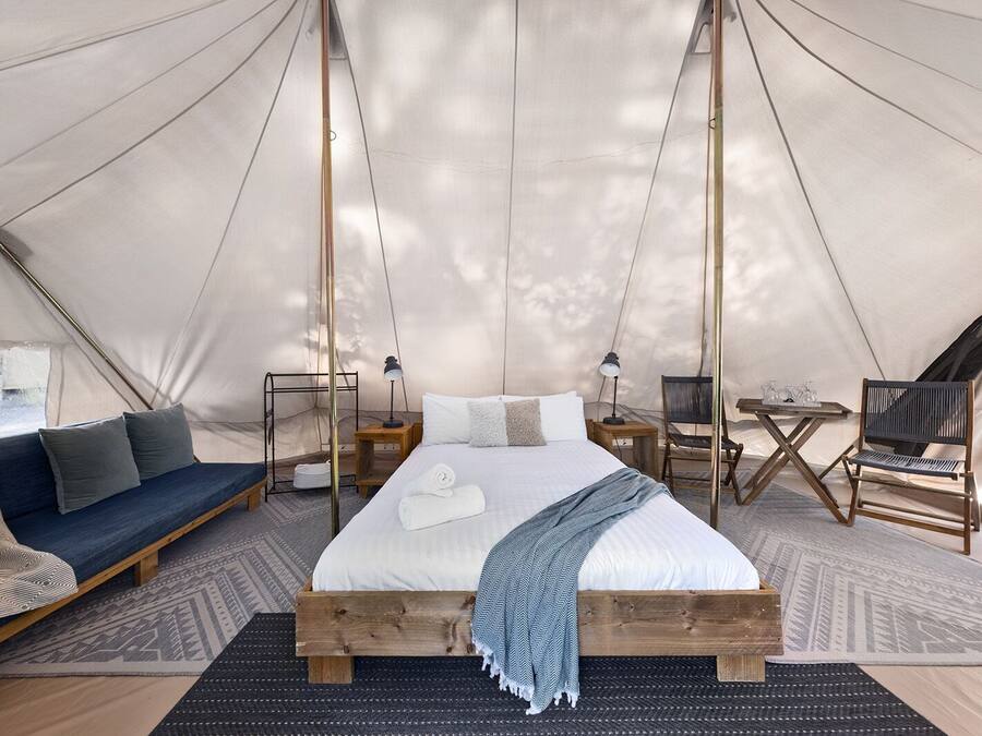 A tented accommodation with a bed, seating area, and a table with chairs.