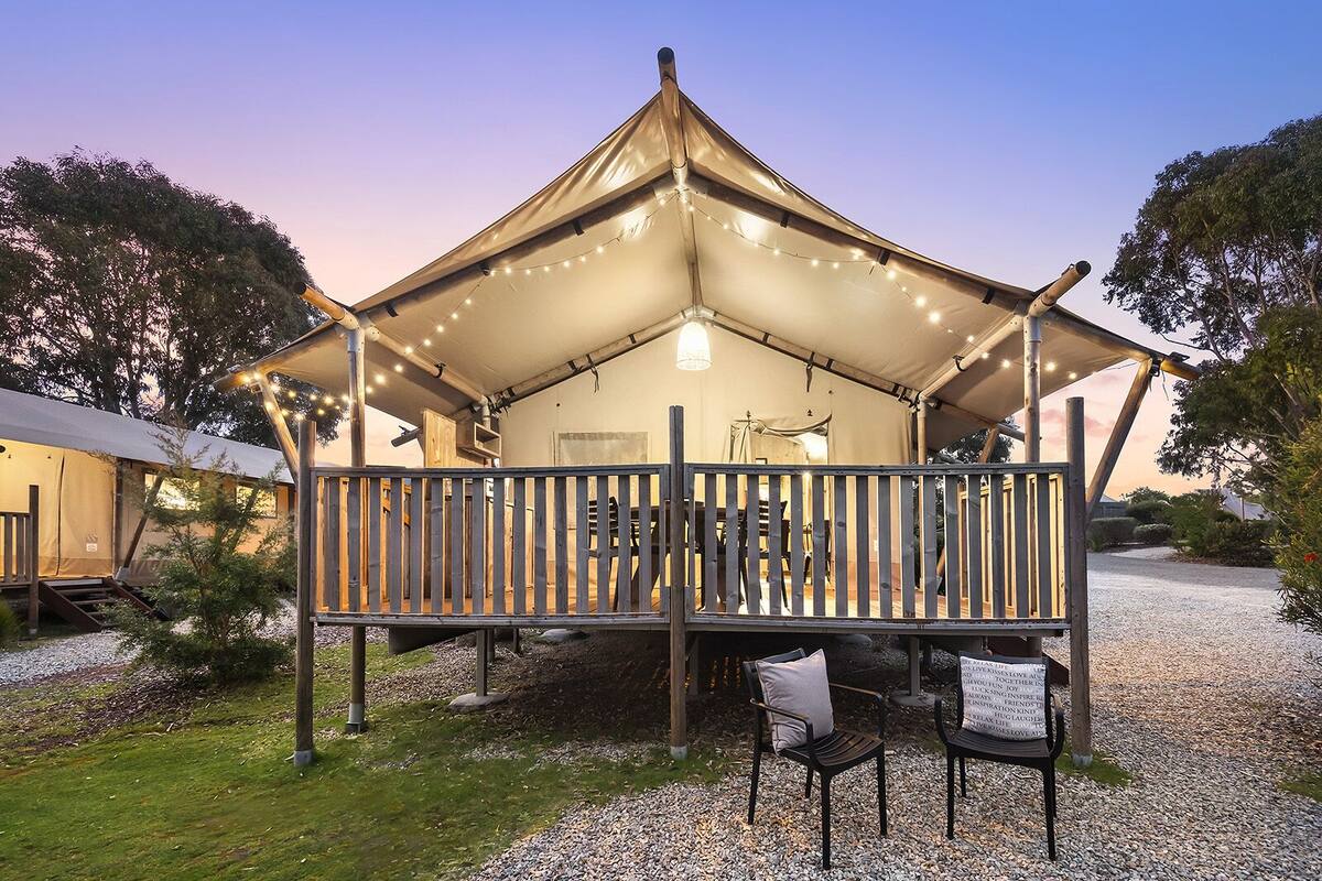 A tented accommodation with a wooden deck, string lights, and a gravel ground.