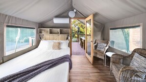 A tented accommodation with a bed, a seating area, and a view of the outdoors. - Scamander Sanctuary Holiday Park (Scamander)