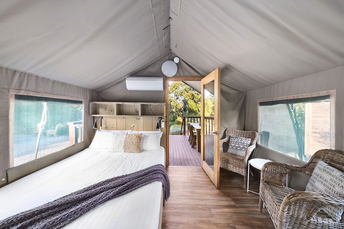 A tented accommodation with a bed, a seating area, and a view of the outdoors.