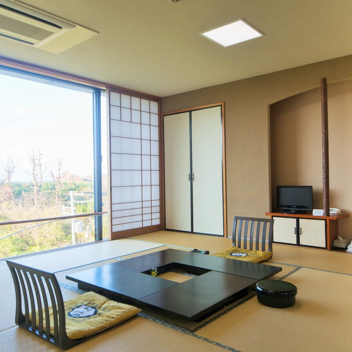 A room with tatami flooring, a low table with cushions, a television on a stand, and a sliding door.