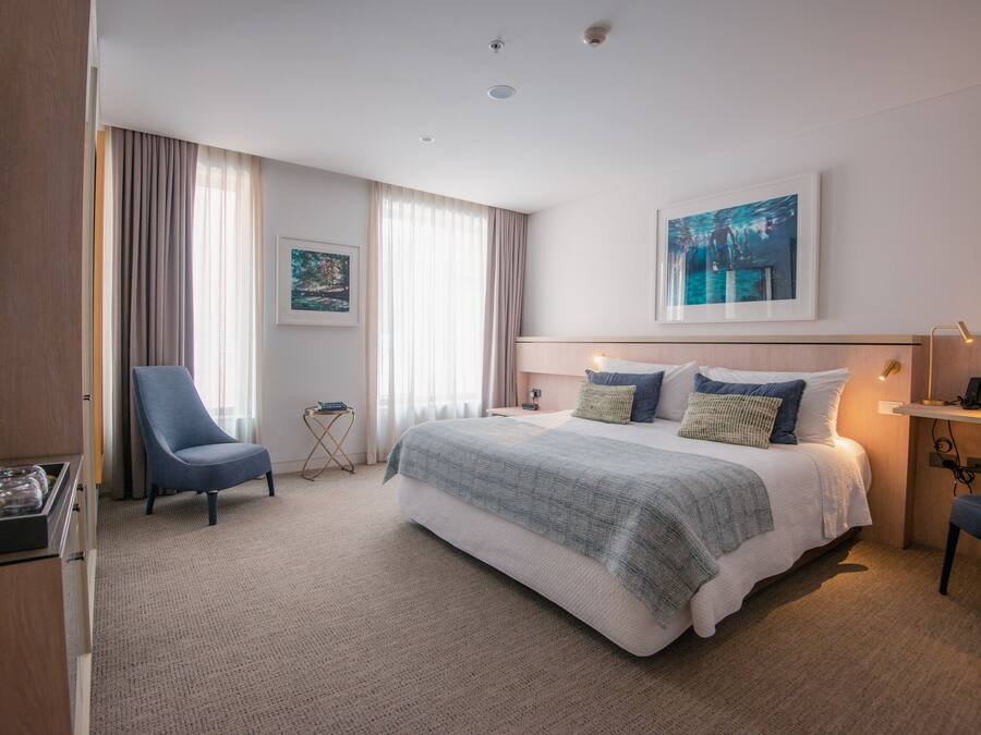 A hotel room with a large bed, a chair, a desk, and a painting on the wall.