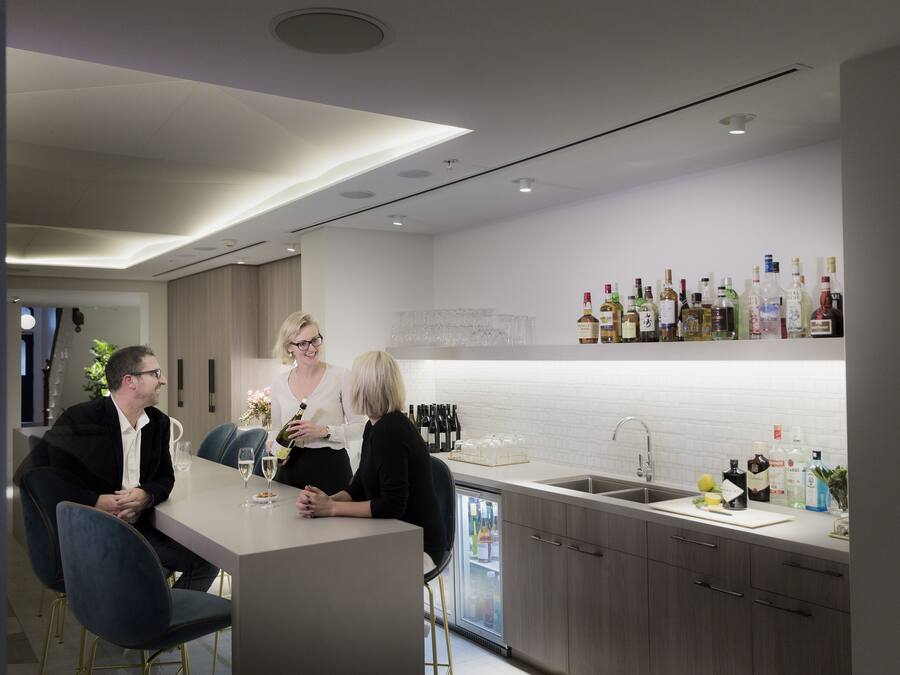 A modern kitchen with a bar area, featuring a wine refrigerator, a variety of bottles, and a clean, minimalist design.