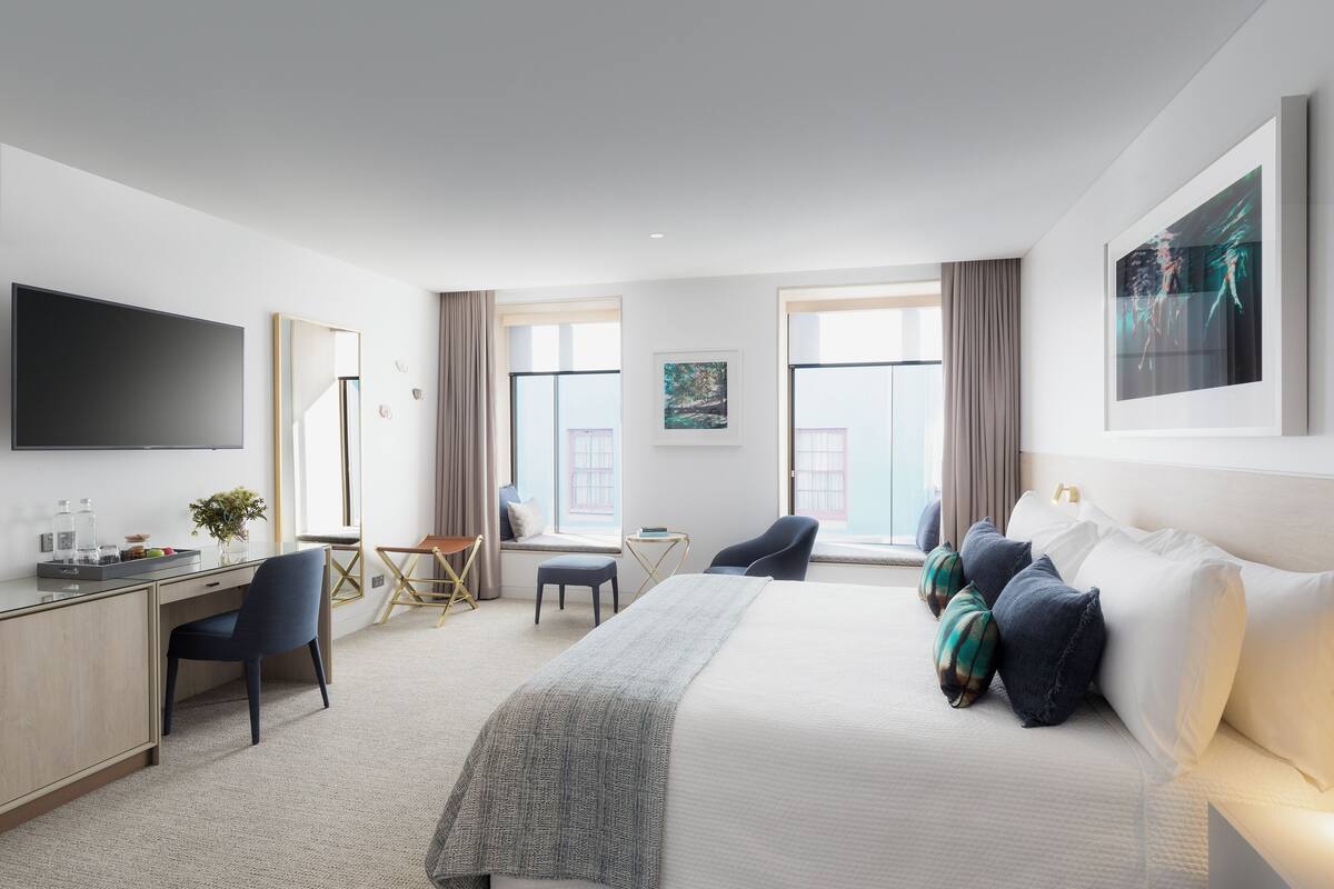 A modern hotel room with a large bed, a desk, a chair, and a TV.