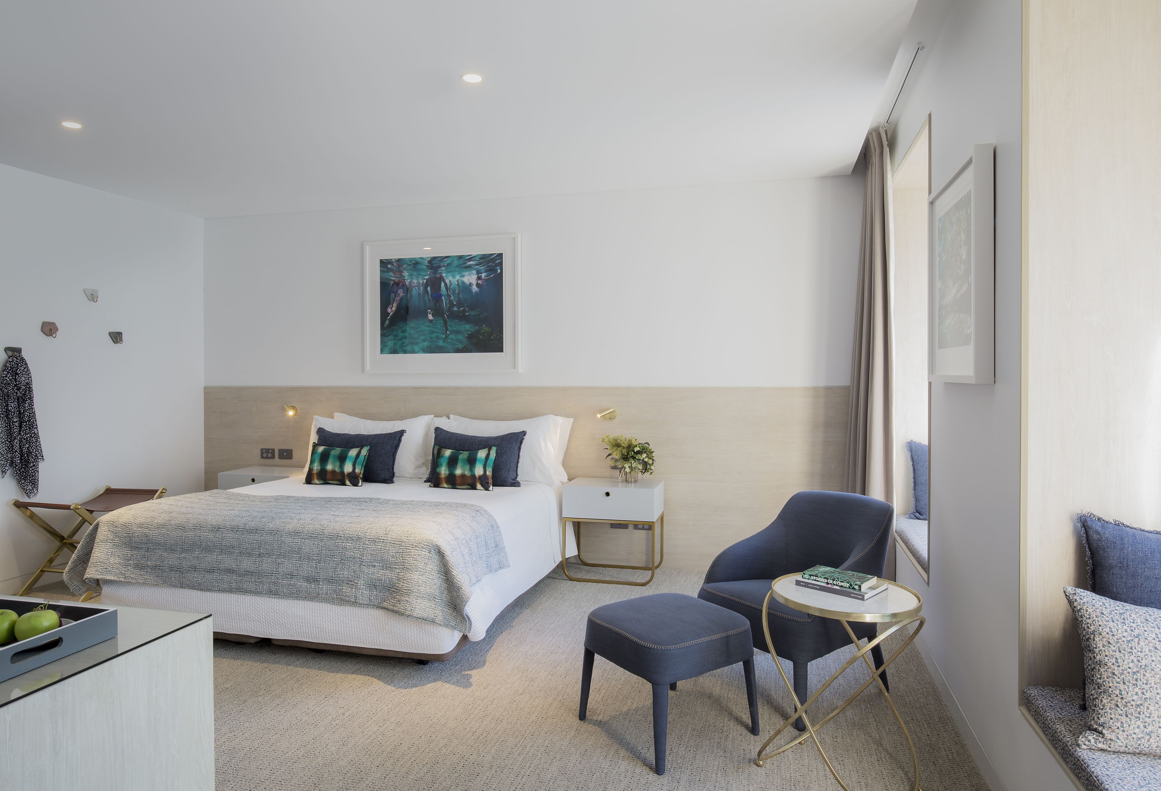 A modern hotel room with a large bed, a desk, a chair, and a small table.