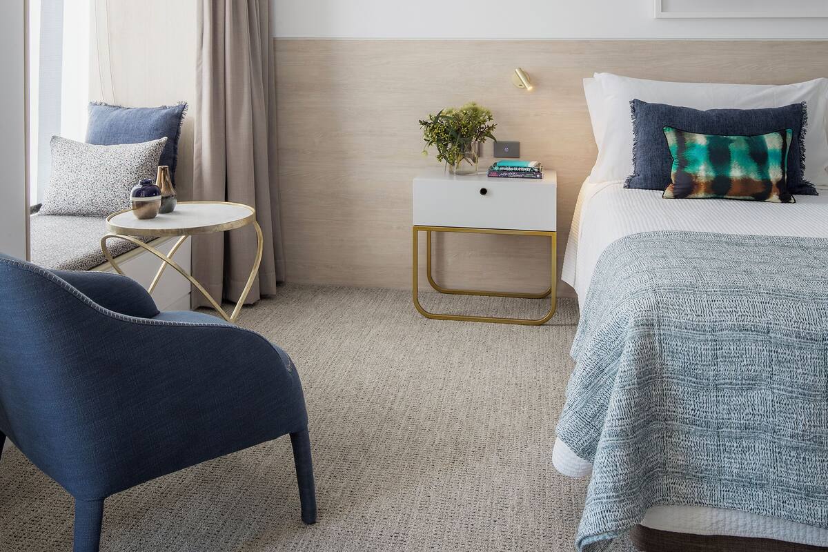 A modern hotel room with a bed, a chair, a nightstand, and a window with curtains.