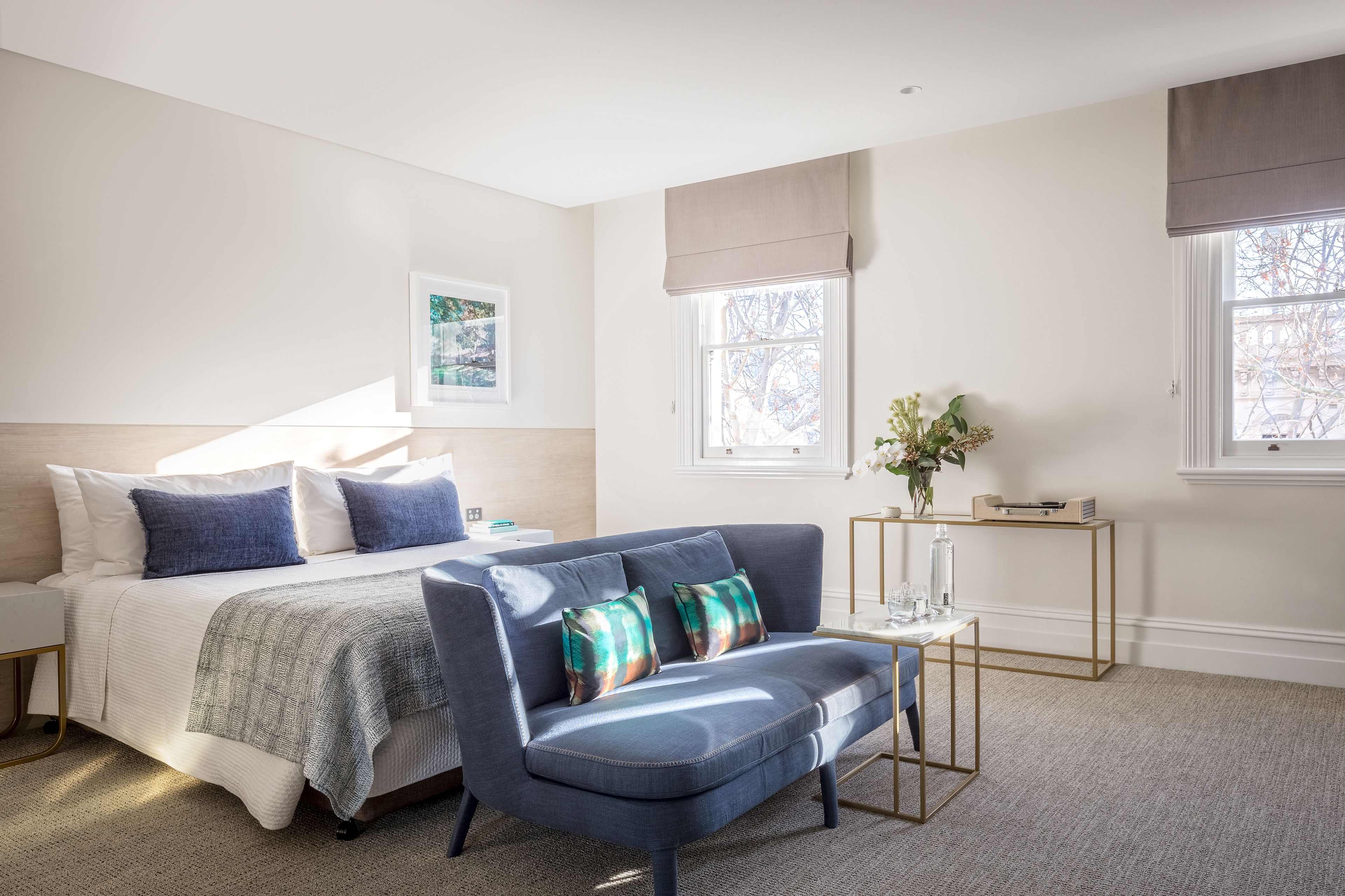 A bedroom with a bed, a blue sofa, a bedside table, and a window with a view of trees.