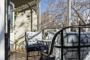 Uma varanda com uma cadeira, uma mesa pequena com uma planta e vista para árvores e céu.
