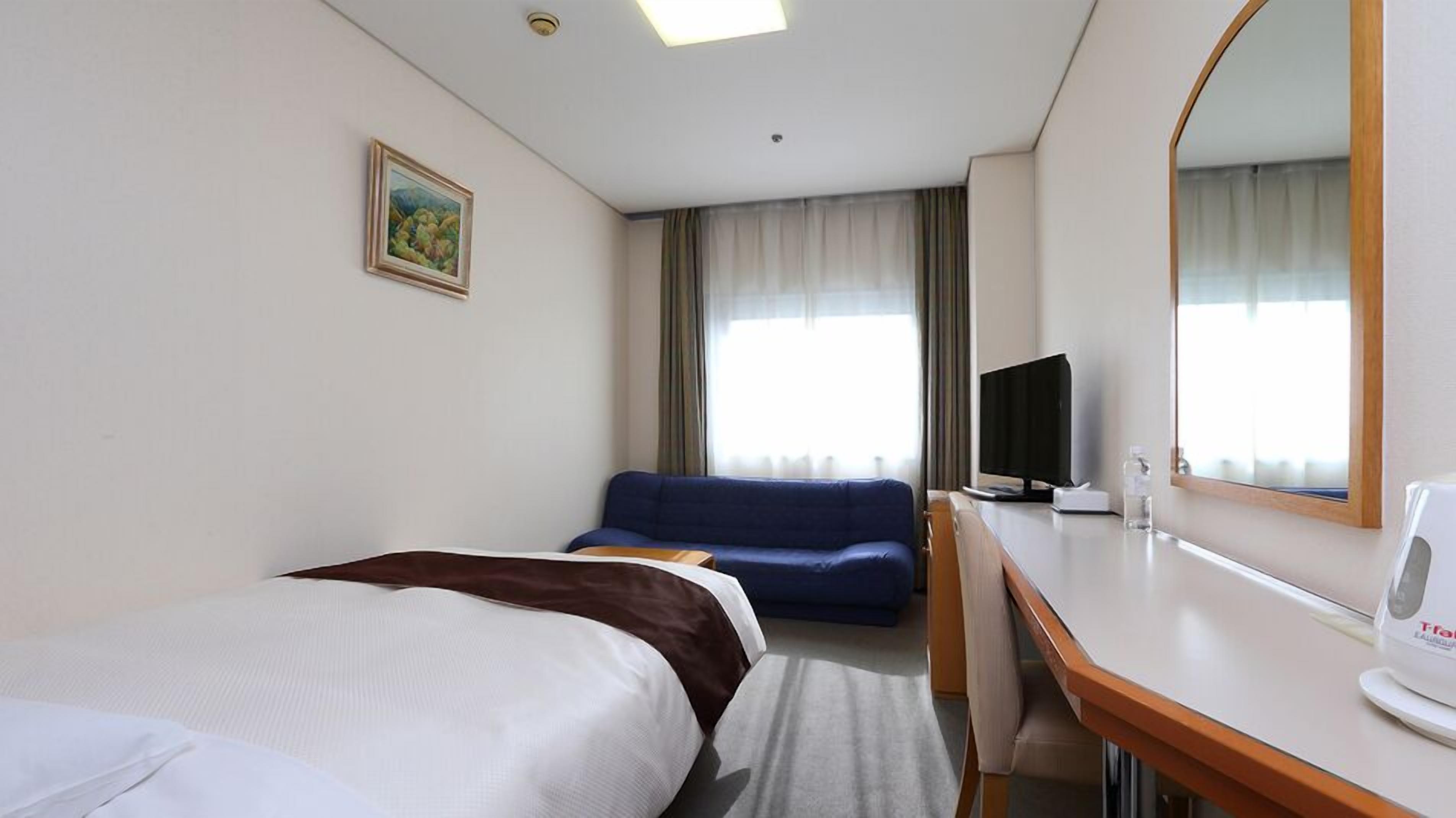 Hotellihuone, jossa on kaksi sänkyä, työpöytä, televisio ja suuri peili.