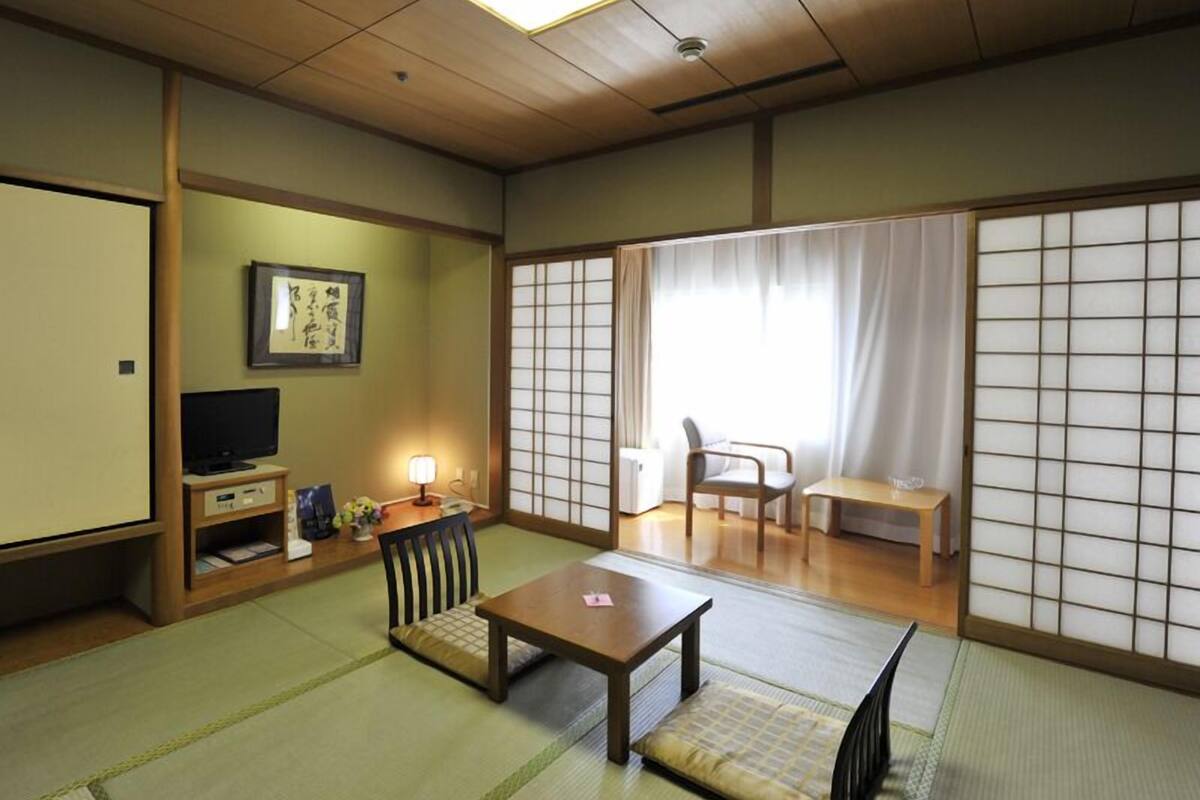 Perinteinen japanilainen huone, jossa on tatamimatto, matala pöytä, televisio ja liukuvat ovet.