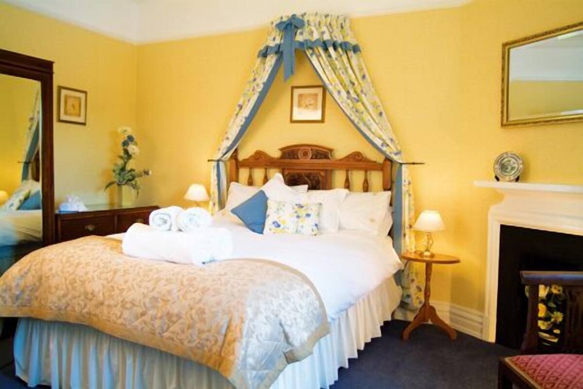 Une chambre d’hôtel avec un lit à baldaquin, une cheminée et un miroir au mur.