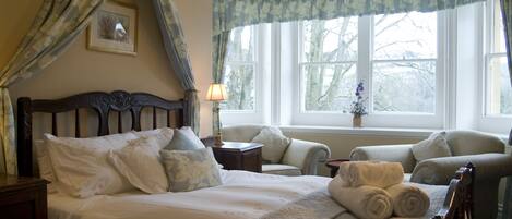 A bedroom with a large bed, two armchairs, a nightstand, and a window with curtains.