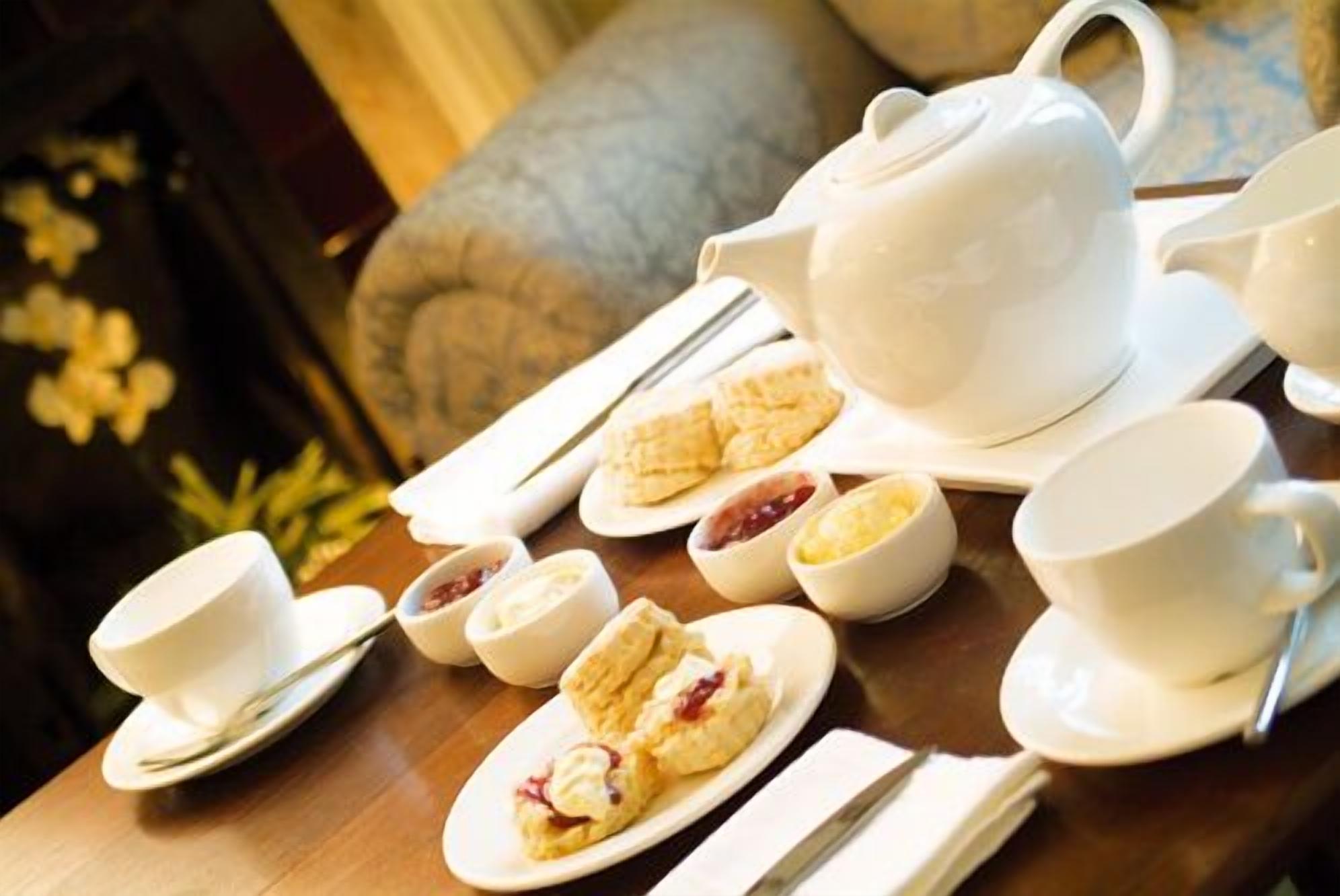 A table set with a white teapot, cups, saucers, and plates with pastries and jams.