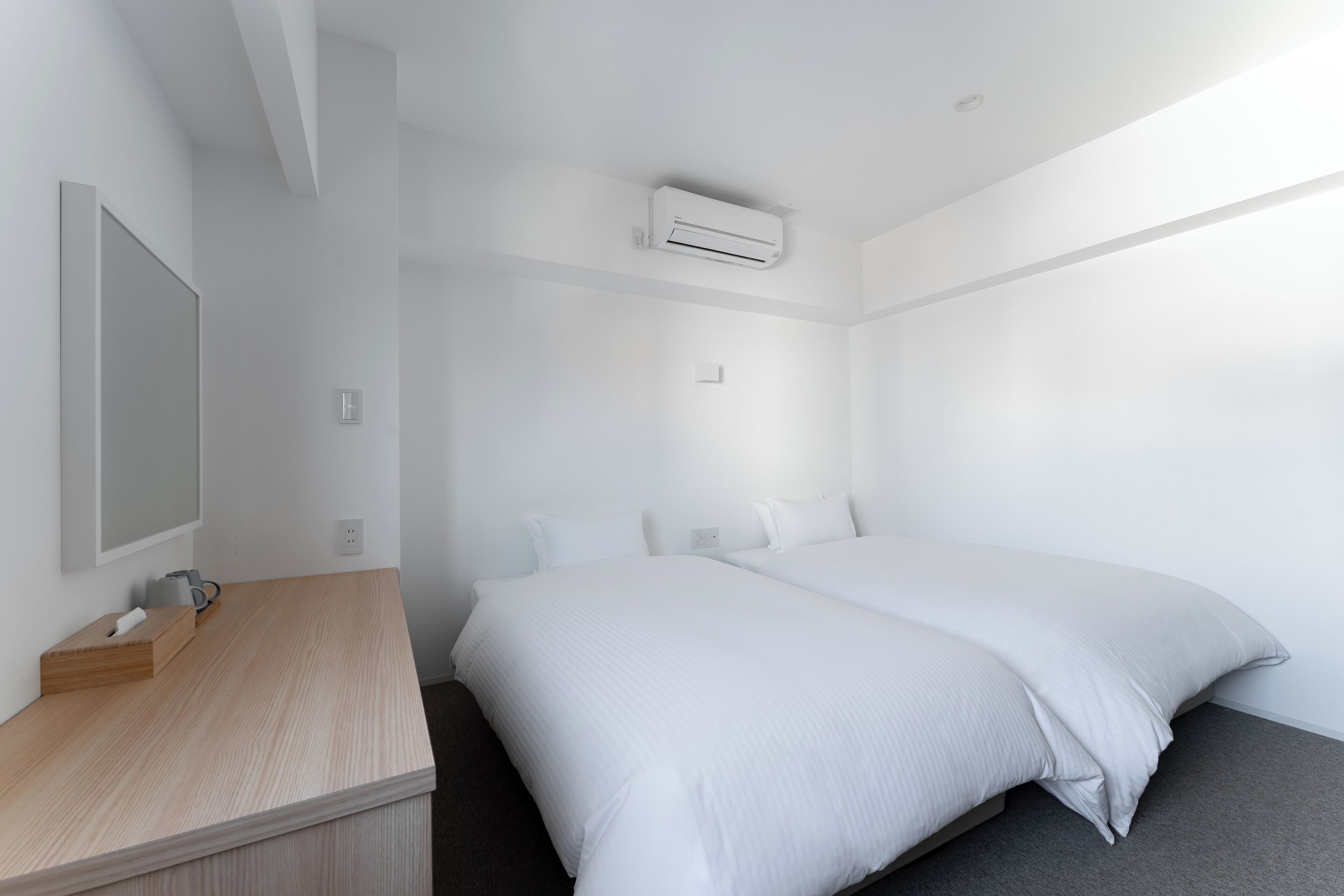Ein modernes Hotelzimmer mit einem großen Bett, einem Nachttisch aus Holz, einem Flachbildfernseher und einer wandmontierten Klimaanlage.