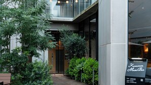 Um edifício moderno com um deck de madeira, vegetação e uma placa indicando 'Karazama Music Bar'.