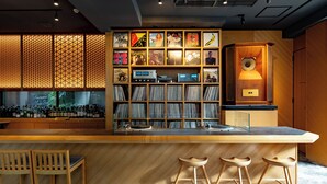 Uma área de bar com balcão de madeira, banquetes e uma estante com discos de vinil.