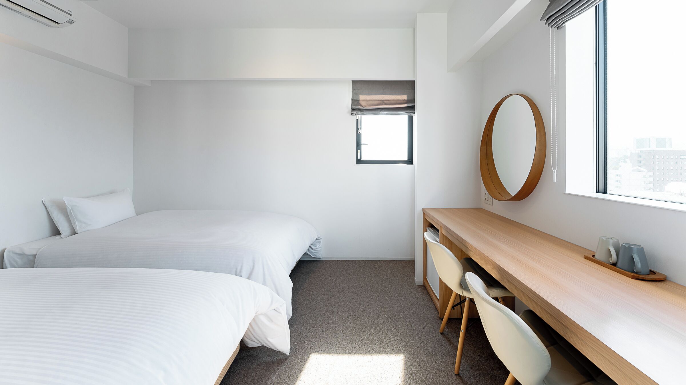 Een hotelkamer met twee bedden, een bureau, een stoel, een spiegel en een raam.